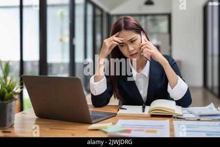 Une jeune employée de bureau sérieuse, une femme assise à un bureau sur le lieu de travail, tenant un téléphone mobile, fait entendre les demandes des clients se sent mécontente Banque D'Images