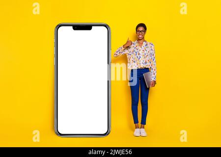 Portrait en longueur de la personne positive montrer le pouce vers le haut espace vide énorme téléphone isolé sur fond jaune couleur Banque D'Images