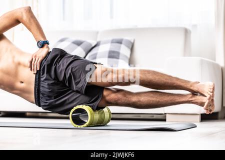 Jeune homme massant le muscle latéral de la cuisse avec rouleau en mousse. Banque D'Images