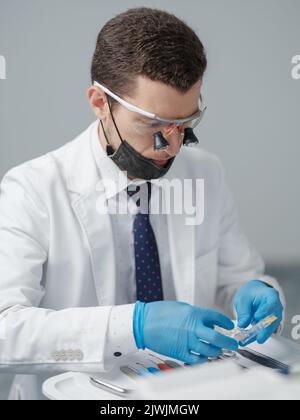 Dentiste de sexe masculin en blouse de laboratoire blanche portant des loupes binoculaires dentaires et vérifiant son équipement médical au cabinet dentaire Banque D'Images