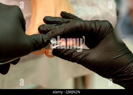 Pédicure professionnelle. Pédicure maître portant des gants en latex coupe les ongles du pied féminin dans le salon de beauté, gros plan Banque D'Images