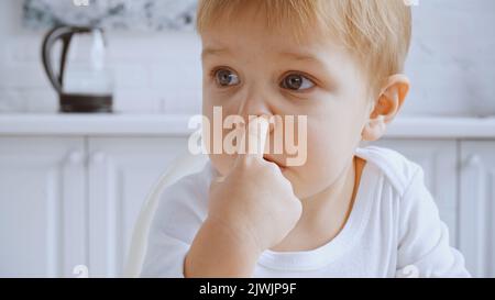 gros plan sur un jeune garçon méchant qui prend le nez et regarde loin Banque D'Images