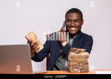 un homme d'affaires africain enthousiaste avec beaucoup d'argent qui fait des appels téléphoniques Banque D'Images