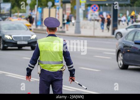 Vue arrière de l'homme anonyme en uniforme de police de la circulation et gilet de sécurité debout près de la route avec des voitures sur la rue de la ville Banque D'Images