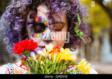 gros plan et vue de face portrait de la jeune femme caucasienne avec la Calavera catrina maquillage avec les yeux fermés et odeur des fleurs à l'extérieur Banque D'Images