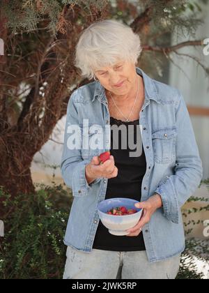 Femme âgée tenant un bol de fraises mûres Banque D'Images