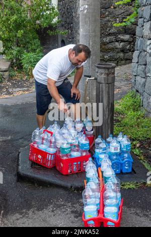 Remplissage des bouteilles d'eau avec de l'eau douce délicieuse provenant d'une fontaine publique dans le village sicilien de Milo, sur les pentes de l'Etna Banque D'Images