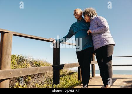 Couple senior joyeux riant avec joie en se tenant sur un pont à pied en bord de mer. Un couple de personnes âgées à la retraite passe un certain temps de qualité ensemble pendant un r Banque D'Images