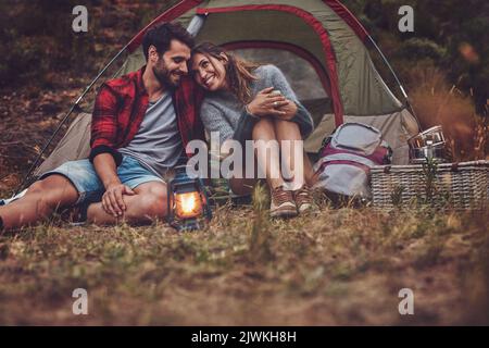 Couple romantique passant du temps de qualité sur un camping vacances. Homme et femme aimant assis à l'extérieur de leur tente le soir avec une lanterne. Banque D'Images