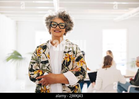 Femme d'affaires mûre souriant à la caméra tout en se tenant dans une salle de réunion. Femme d'affaires heureuse assistant à une réunion avec son équipe dans une femme d'affaires Banque D'Images