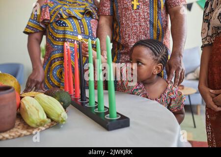 Petite fille africaine éclairant des bougies sur la table tout en célébrant les vacances de Kwanzaa avec sa famille Banque D'Images