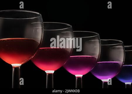 Verres multicolores avec différents vins coctail - violet bleu rouge sur fond noir verres d'affilée. Banque D'Images