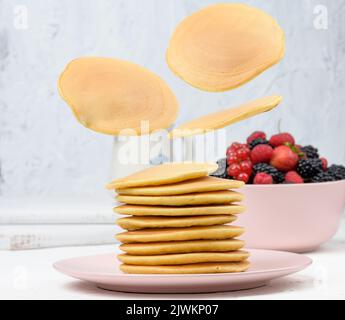 Une pile de crêpes cuites avec des fruits dans une assiette ronde sur une table blanche Banque D'Images