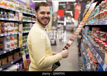 client satisfait regardant la caméra dans le magasin de matériel à côté des rangées de peinture de rénovation Banque D'Images