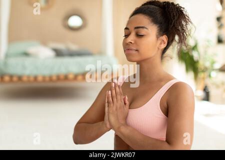 Harmonie de l'esprit. Portrait de dame noire calme méditant avec les yeux fermés, gardant les mains dans le geste naste, espace libre Banque D'Images