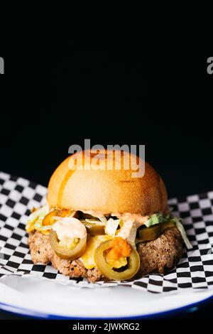 Bouchez le cheeseburger avec les légumes et le jalapeños sur une assiette blanche sur un fond noir Banque D'Images