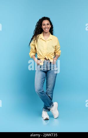Portrait de la jeune femme positive dans une tenue décontractée à la mode debout et regardant l'appareil photo sur fond bleu Banque D'Images