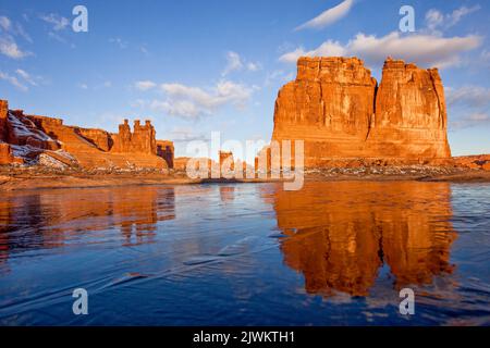 L'orgue, dans les tours du palais de justice, se reflète dans un nid de poule enneigé surgelé éphémère dans le parc national d'Arches, Moab, Utah. Banque D'Images