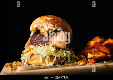 Hamburger de bacon avec laitue accompagné de patates douces sur une table en bois et sur fond noir Banque D'Images