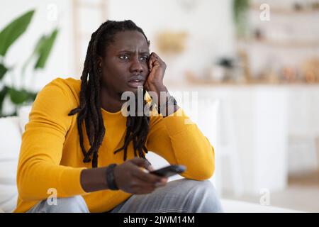 Programme d'alésage. Portrait d'un jeune homme noir ennuyé regardant la télévision à la maison Banque D'Images