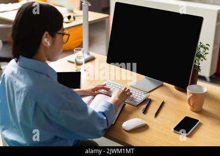 Femme coréenne méconnaissable utilisant un ordinateur avec écran vide dans Office Banque D'Images