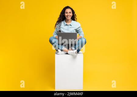 Femme gaie du Moyen-Orient utilisant un ordinateur portable sur fond jaune Banque D'Images