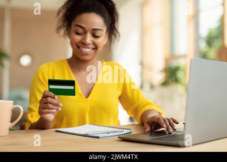 Paiement et remboursement faciles. Femme noire souriante faisant des achats en ligne à la maison en utilisant un ordinateur portable et une carte de crédit Banque D'Images