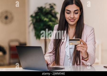 Belle jeune femme d'affaires brune, utilisant son ordinateur portable et de la glacer à sa carte de crédit au bureau. Banque D'Images
