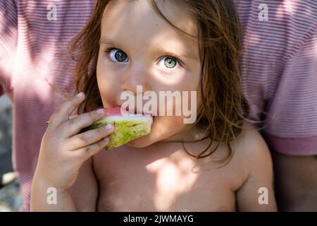 Portrait d'un bébé mignon. Le gamin mange une pastèque et regarde la caméra . Style de vie. Franc. Le concept de vacances familiales actives. Vue avant. Gros plan. Banque D'Images