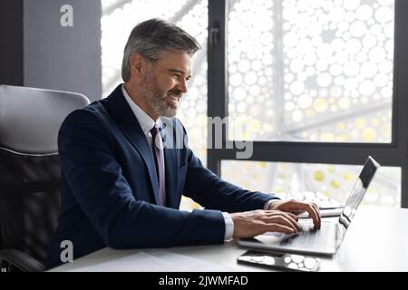 Un esprit d'entreprise réussi. Beau homme d'affaires d'âge moyen travaillant avec un ordinateur portable au bureau Banque D'Images