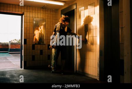 homme appuyant sur le bouton de l'ascenseur dans la ville avec son skateboard Banque D'Images