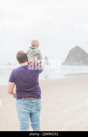 Blond, un tout-petit caucasien est assis sur les épaules du père à Cannon Beach. Banque D'Images