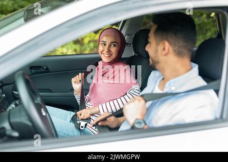Souriante jeune femme du Moyen-Orient dans le hijab et homme bouclent les ceintures de sécurité, profiter de voyage en voiture Banque D'Images
