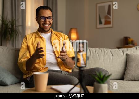 Joyeux jeune enseignant afro-américain donnant des cours ou des conférences en ligne, en utilisant le smartphone à la maison, l'espace de copie Banque D'Images