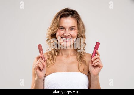 Maquillage tendance. Belle femme d'âge moyen tenant deux brillants à lèvres dans les mains Banque D'Images