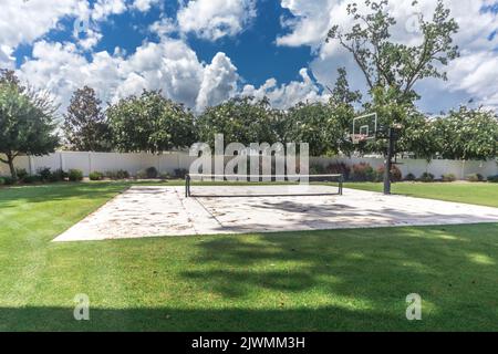 Une grande cour avec de l'herbe verte et un terrain de basket-ball qui a été fait dans un terrain de pickleball à la maison Banque D'Images