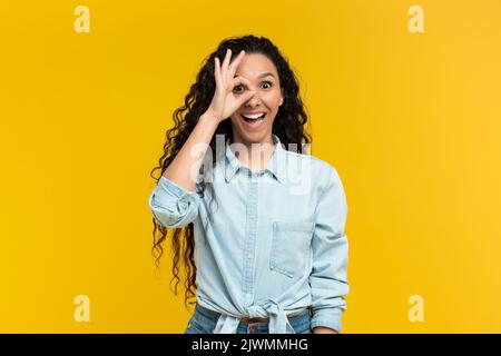 Jeune femme excitée montrant un geste correct près de son œil sur fond jaune studio Banque D'Images