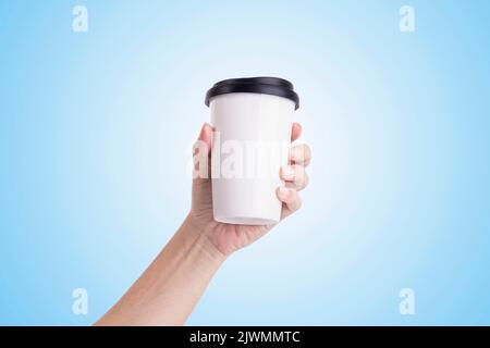 Main mâle tenant une tasse à café blanche isolée sur fond bleu clair. Banque D'Images