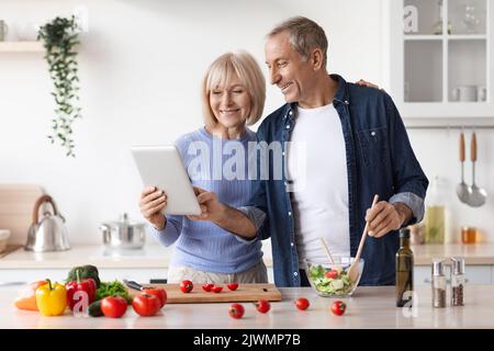 Un couple senior lisant un blog alimentaire sur une tablette numérique, la cuisine Banque D'Images