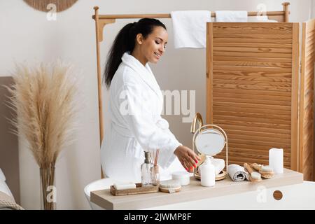 Femme noire utilisant des produits cosmétiques assise sur une baignoire dans la salle de bains Banque D'Images