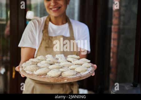 Accent sélectif sur les boulettes ou le varéniki sur une planche en bois dans les mains d'une femme charmante ménagère dans le tablier du chef Banque D'Images