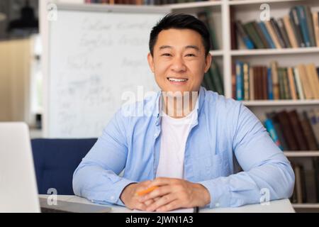 Joyeux enseignant asiatique Homme souriant assis près d'un ordinateur portable sur le lieu de travail Banque D'Images