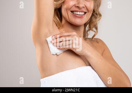 Gros plan sur une femme d'âge moyen souriante qui essuit une aisselle avec une serviette Banque D'Images