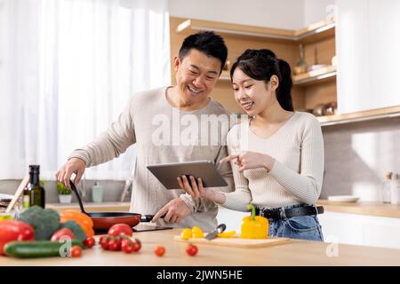 Un couple asiatique souriant vérifie les recettes sur Internet Banque D'Images