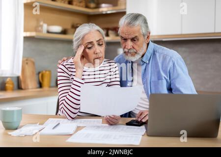 Les conjoints âgés contrariés lisant des documents tout en calculant le budget familial dans la cuisine Banque D'Images