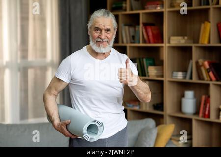 Homme de haut niveau gai s'exerçant à la maison, tenant un tapis de yoga Banque D'Images