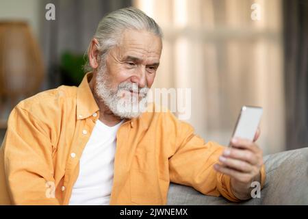 Gros plan d'un vieil homme positif utilisant un téléphone portable à la maison Banque D'Images