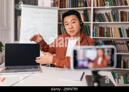 Professeur d'Asie masculin ayant une conférence en ligne montrant l'écran d'ordinateur portable en intérieur Banque D'Images