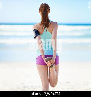 Étirement de ses muscles. Vue arrière d'une jeune femme qui s'étire avant un travail sur la plage. Banque D'Images