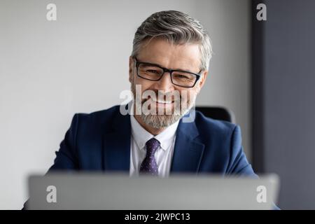 Beau barbu homme d'affaires d'âge moyen portant des lunettes travailler avec un ordinateur portable au bureau Banque D'Images
